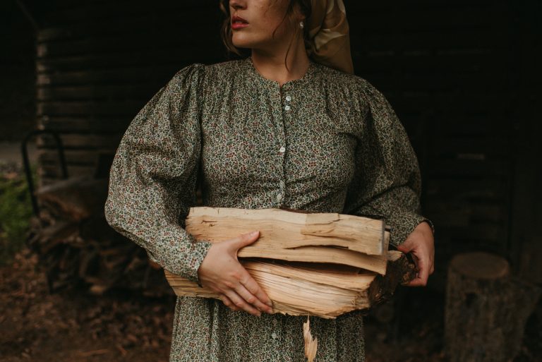 woman in a rustic barn with chopped wood wearing Doen green dress