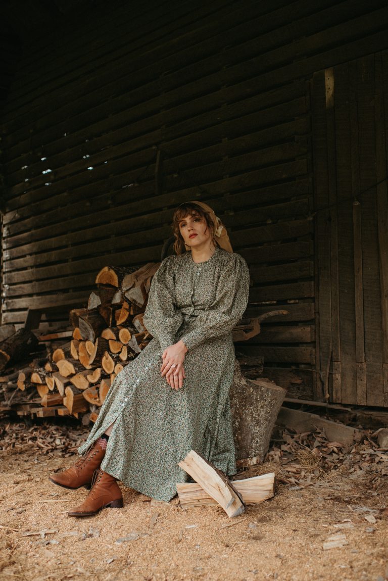 woman in a rustic barn with chopped wood wearing Doen green dress