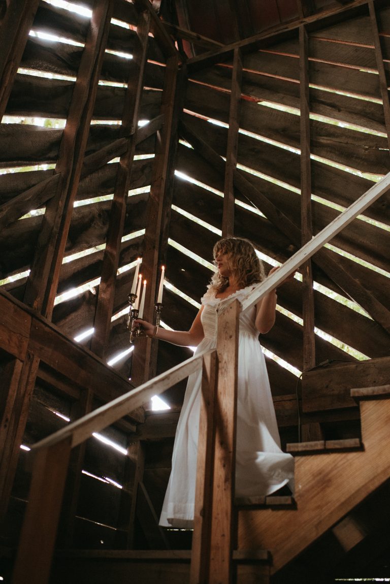 Woman in cottagecore fashion Doen dress walking down barn staircase with candles