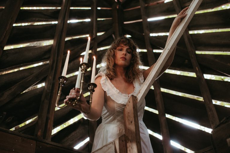 Woman in cottagecore fashion Doen dress walking down barn staircase with candles