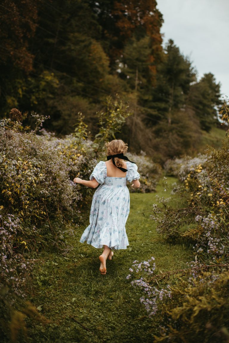 Woman in Selkie La Belle Etoile French Puff Dress running in field next to cottagecore barn