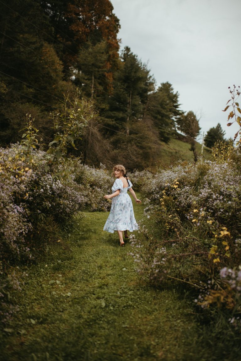 Woman in Selkie La Belle Etoile French Puff Dress running in field next to cottagecore barn