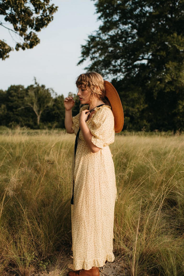 Woman in cottage core Christy Dawn dress with Behida Dolic bolero hat in a field