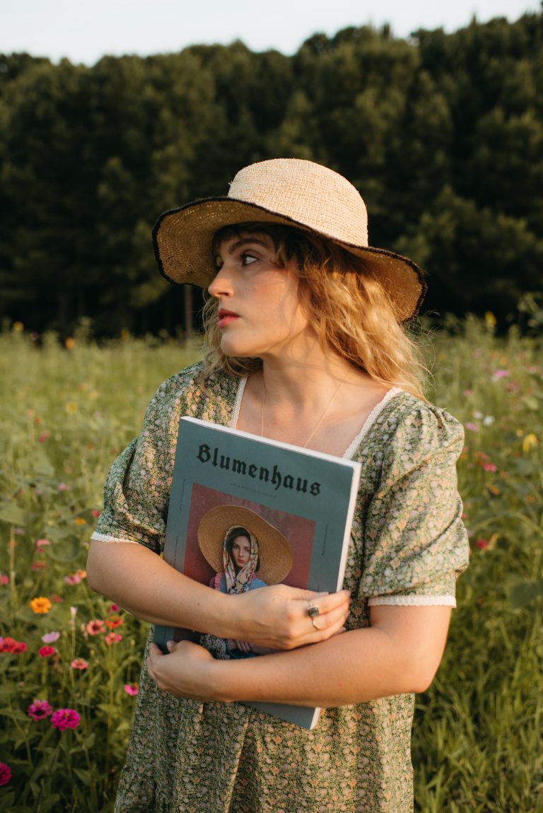 Women in green Christy Dawn dress holding Blumenhaus magazine in a flower field